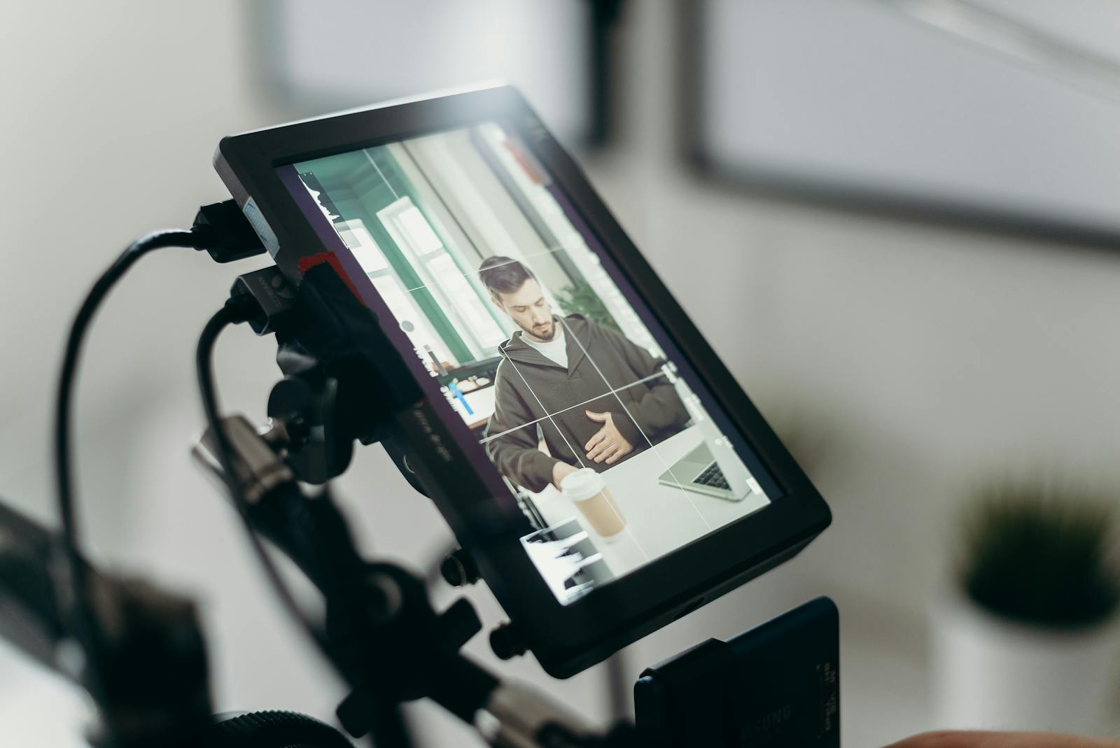 A videographer captures a man working at a desk through a camera screen in a modern office environment.